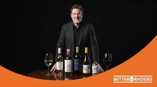 Better Rhodes CEO standing behind a curated lineup of premium non-alcoholic bottles and wine glasses