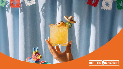 Hand holding a zero-proof margarita with a salted rim, lime garnish and mini sombrero