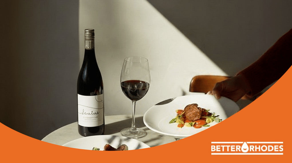 Bottle and glass of red wine served with a plated meal on a sunlit table