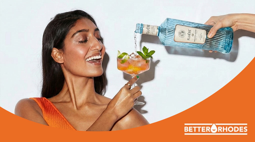 Woman pouring non-alcoholic spirit into an orange spritz cocktail with lime and mint garnish